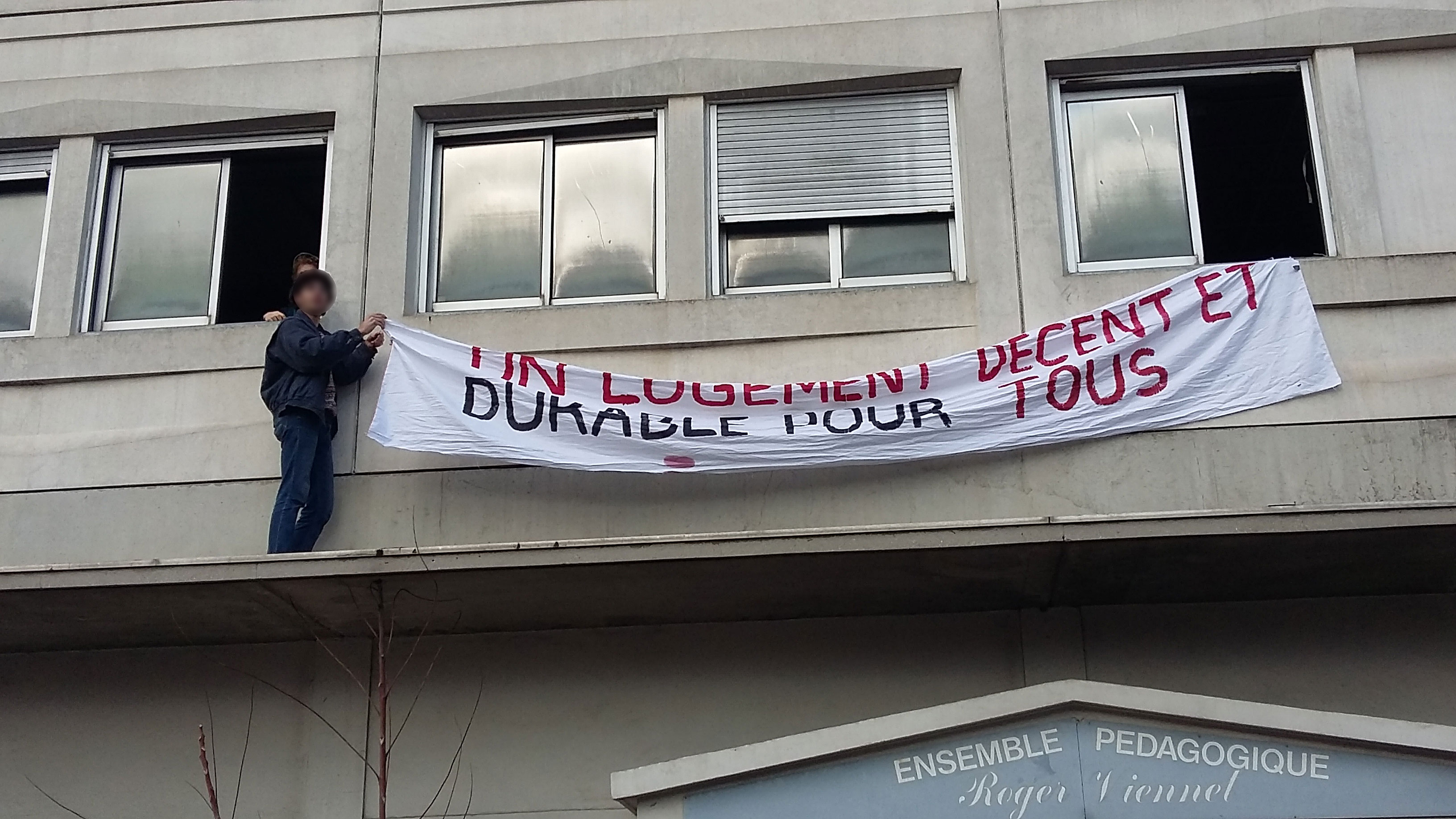 Deux étudiants mettent en place une banderole sur le squat de Vileurbanne