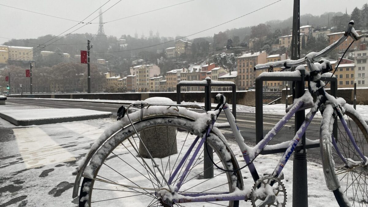 Un vélo enneigé au premier plan, sur les quais de saone à Lyon. Au loin, on distingue fourvière.